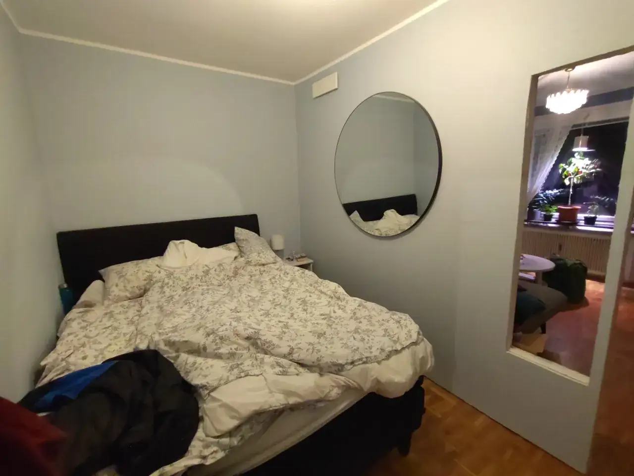 Sovrum med en stor säng, spegel på väggen och en öppen dörr som visar ett annat rum. Känns som dålig luft i sovrummet.