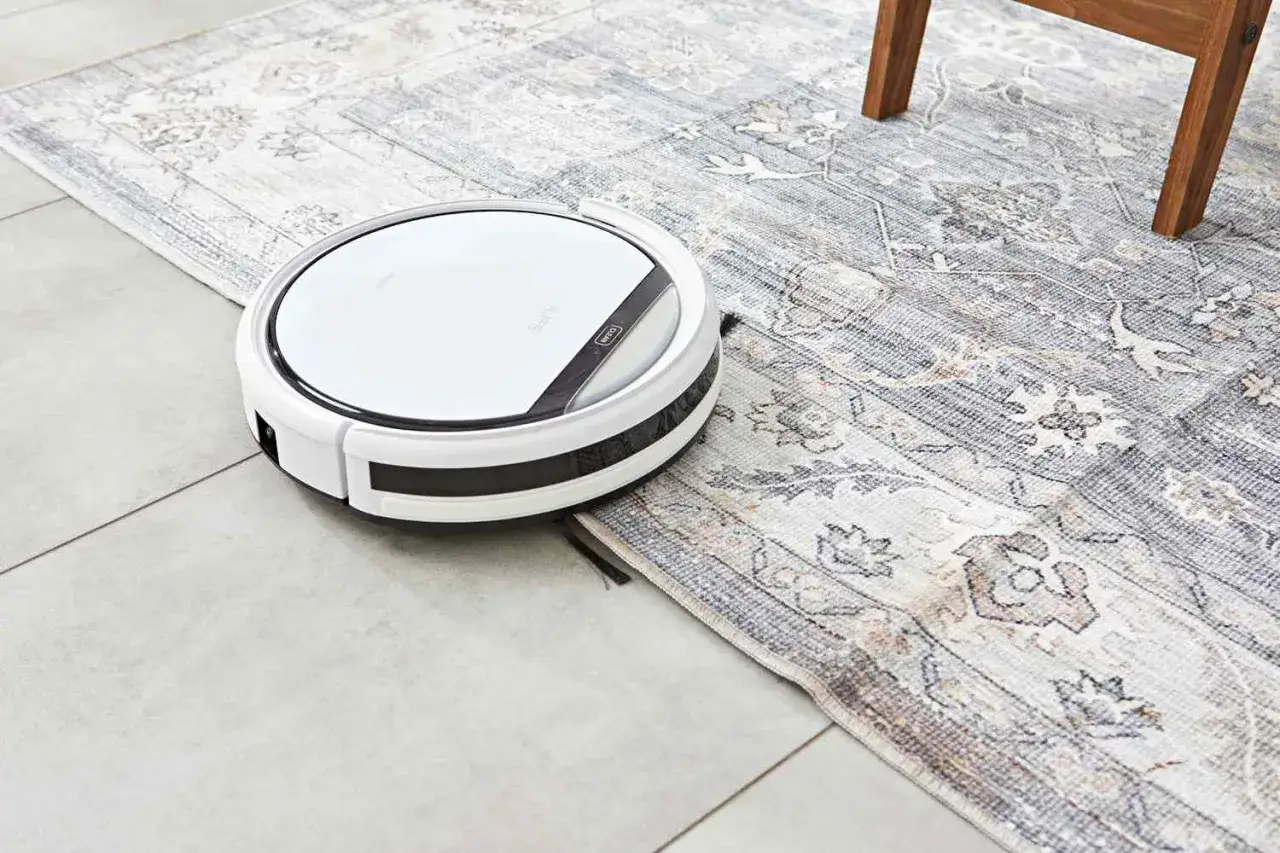 En vit robotdammsugare navigerar &ouml;ver en m&ouml;nstrad matta, redo att ta sig an dammet.