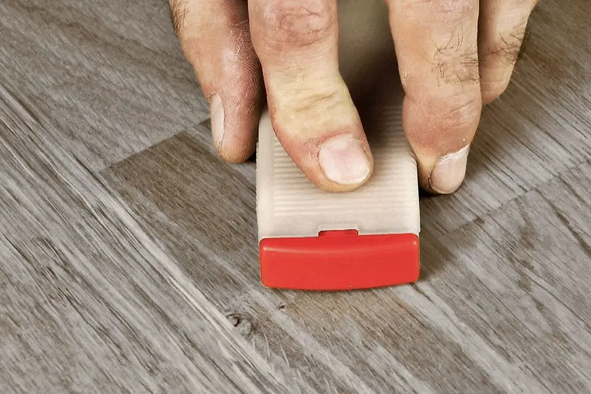 Fingrar trycker ner en kil för att laga laminatgolv.